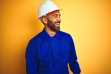 Handsome Indian Worker Man Wearing Uniform And Helmet Over Isolated Yellow Background Looking Away To Side With Smile On Face, Natural Expression. Laughing Confident.