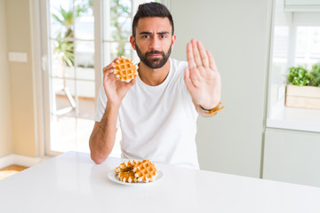 Poster - Handsome hispanic man eating sweet belgian waffle pastry with open hand doing stop sign with serious and confident expression, defense gesture