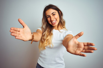 Canvas Print - Young beautiful woman wearing casual white t-shirt over isolated background looking at the camera smiling with open arms for hug. Cheerful expression embracing happiness.