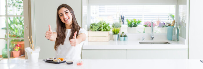 Wide angle picture of beautiful young woman eating asian sushi from delivery approving doing positive gesture with hand, thumbs up smiling and happy for success. Looking at the camera, winner gesture.