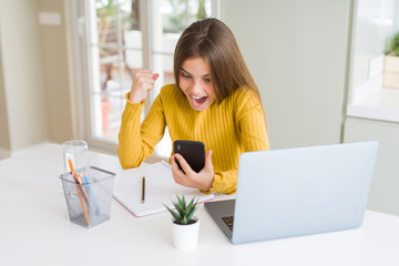 Wall Mural - Beautiful young girl kid using smartphone and computer laptop screaming proud and celebrating victory and success very excited, cheering emotion