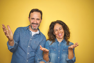 Canvas Print - Beautiful middle age couple together standing over isolated yellow background smiling cheerful offering hands giving assistance and acceptance.