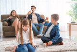 Fototapeta Nowy Jork - Sad little children sitting on floor while addicted parents drinking alcohol at home