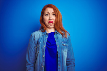 Poster - Young beautiful redhead woman wearing denim shirt standing over blue isolated background depressed and worry for distress, crying angry and afraid. Sad expression.