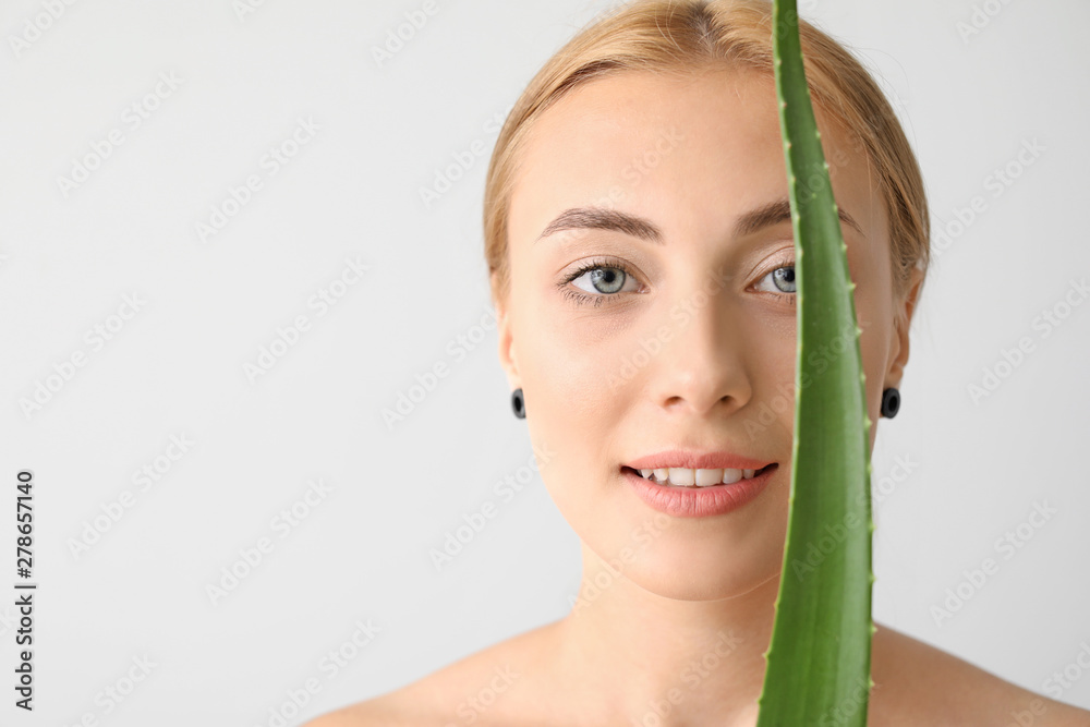 Beautiful young woman with aloe vera on light background