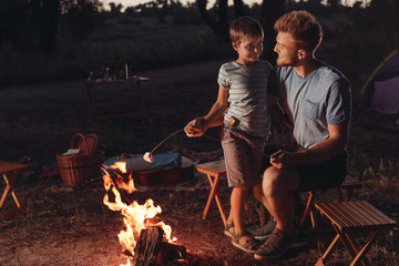 Sticker - Father and son roasting marshmallow over campfire in evening