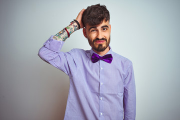 Sticker - Young man with tattoo wearing purple shirt and bow tie over isolated white background confuse and wonder about question. Uncertain with doubt, thinking with hand on head. Pensive concept.