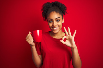 Young african american woman drinking a cup of coffee over isolated red background doing ok sign with fingers, excellent symbol