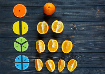 Wall Mural - Сolorful math fractions and oranges as a sample on dark wooden background or table. Interesting creative funny math for kids. Education, back to school concept. Geometry and mathematics materials.