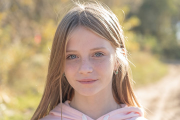 Beautiful blonde young girl with freckles outdoors on nature background in autumn, close up portrait