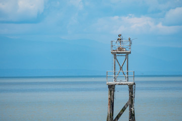  two osprey resting on their nest built on top of a watch tower near the cost with mountain and cloud over the horizon under blue sky