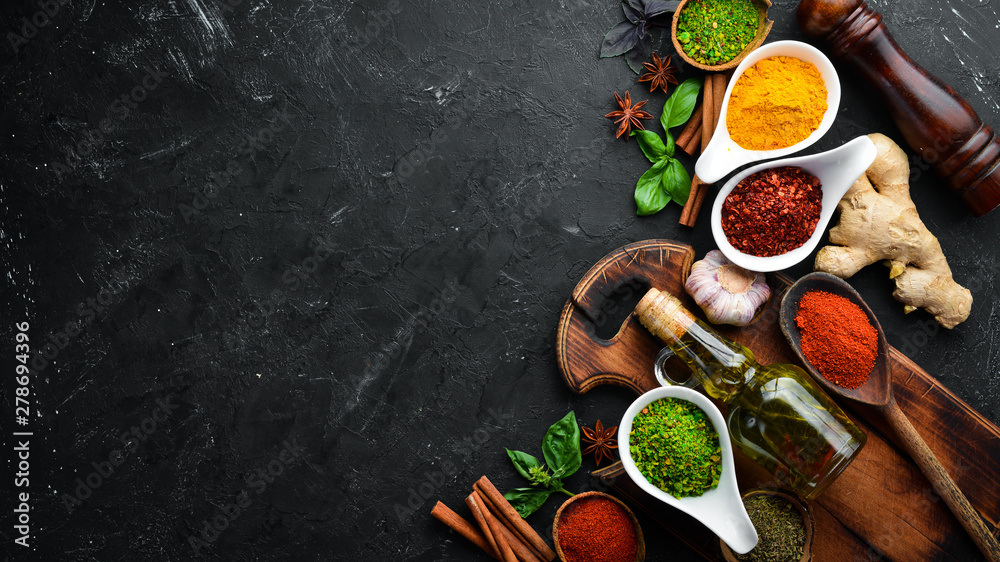 Colorful herbs and spices for cooking. Indian spices. On a black stone background. Top view. - obrazy, fototapety, plakaty 