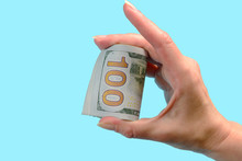 A Hand Is Holding Dollar Bills Rolled Into A Roll On A Blue Background