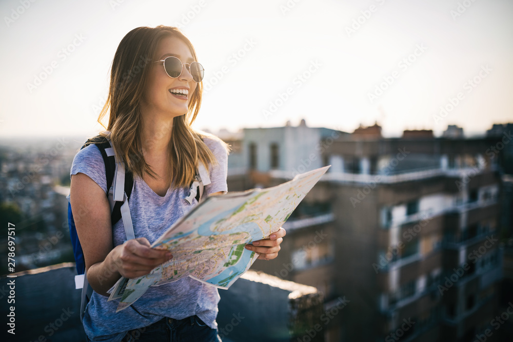 Happy young woman with a city map and a backpack travelling - obrazy, fototapety, plakaty 