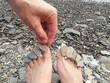 A man puts small stones on the toes of a woman. Feet on the stony bank of the river. Small stones lying on the toes. Сreative pedicure. Rocky shore. Female feet and man's hand closeup.  The weekend.