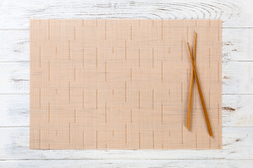 two sushi chopsticks with empty brown bamboo mat or wood plate on white wooden Background Top view with copy space. empty asian food background