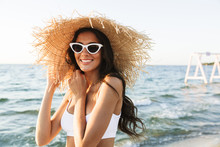 Photo Of Joyful Brunette Woman In Swimsuit And Straw Hat Smiling While Walking By Seaside