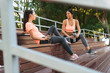 © Drobot Dean - Image of slim women talking and drinking water from bottles while sitting on bench in sports ground