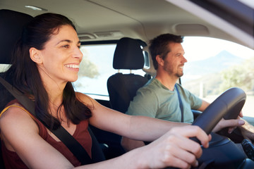 Wall Mural - Mid adult white woman driving car, husband beside her in front passenger seat, close up, side view