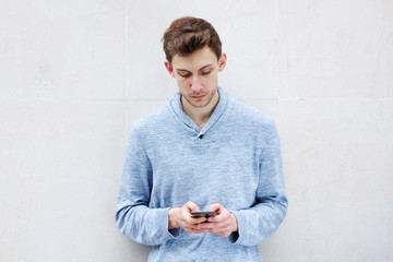 Wall Mural - serious young man looking at cellphone by wall