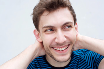 Wall Mural - Close up handsome young man smiling with hands behind head by white wall