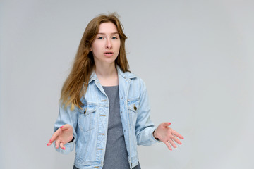 Portrait to waist of a young pretty brunette girl woman with beautiful long hair on a white background in a jacket from jeans. He talks, smiles, shows his hands with emotions in various poses.