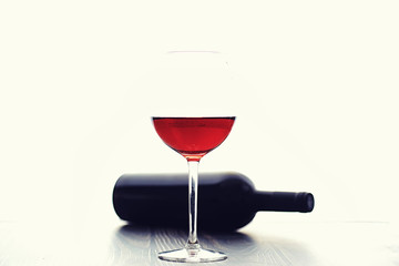 A glass of red dry wine on the table. Dark bottle and glass of wine.