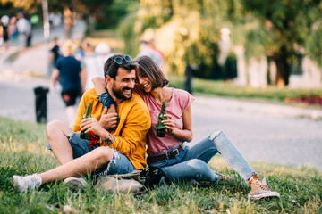 Wall Mural - Young happy couple enjoying a park with beer in hand during the summer