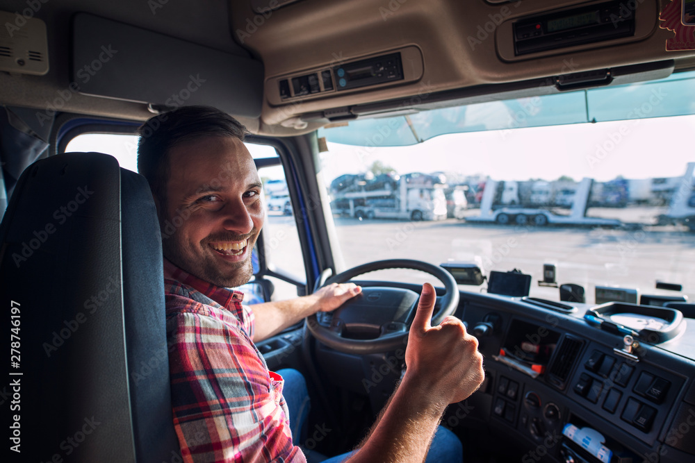 Portrait of truck driver sitting in his truck holding thumbs up. Transportation and trucking services. - obrazy, fototapety, plakaty 