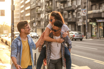 Group of friends hangout at the city street.They embrace each other and laughing.One man carrying female friend on his back.