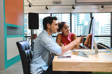 medium side view shot of caucasian graphic design and coworker in smart casual wear talking and working on computer in creative office with happy and smiling face