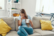 © gstockstudio - Ill young woman blowing nose and sneezing while sitting on the sofa at home