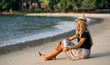 © Artem Markin - A girl in a straw hat sits on the morning beach. Modern girl on vacation