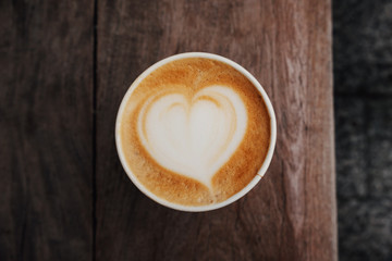 Wall Mural - Fresh hot cappuccino coffee in a paper cup with beautiful latte art in the shape of heart on wooden background. Coffee to go.