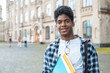 © Oleksandr - Portrait of a young African American student black man the background of college. Smiling teenage male mixed race keeps books standing near the university.