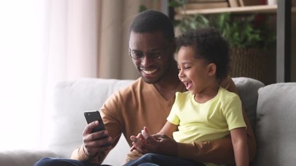 Wall Mural - Happy african dad and little son laughing looking at phone