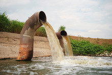 Wastewater From Two Large Rusty Pipes Merge Into The River In Clouds Of Steam