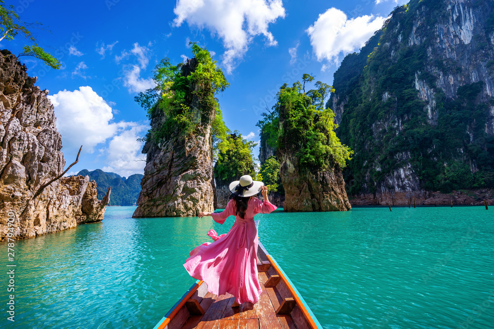 Beautiful girl standing on the boat and looking to mountains in Ratchaprapha Dam at Khao Sok National Park, Surat Thani Province, Thailand. - obrazy, fototapety, plakaty 
