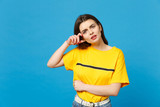 Fototapeta  - Portrait of displeased puzzled young woman in vivid casual clothes looking camera, keeping hand near face isolated on bright blue background in studio. People lifestyle concept. Mock up copy space.