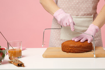 Wall Mural - Close up cropped hands of chef cook confectioner or baker in apron white t-shirt cooking, cutting cake with tool at table isolated on pink pastel background in studio. Mock up copy space food concept.