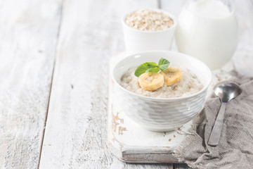 Wall Mural - Bowl of oatmeal porridge with banana on white wooden rustic table, healthy breakfast, diet food.