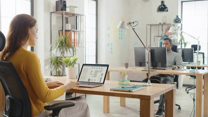 Over the Shoulder: Female Engineer Developer Sitting at Her Desk Using Laptop with Hardware Microchip Design. Office where Diverse Team of Young Professionals Work on Computers