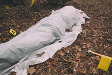 Victim Of A Violent Crime Under A Sheet In A Rural Yard. With Evidence Markers And Murder Weapon.