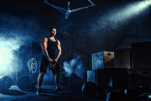 Muscular Attractive Caucasian Bearded Tasttoed Man Lifting Kettlebell In A Gym. Weight Plates, Dumbbell And Tires In Smoke Background.