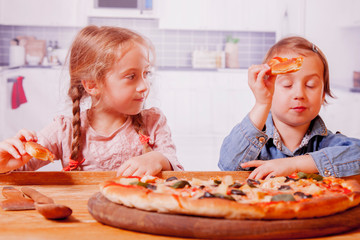 Two little female friends holding pizza slices. Happy children having fun eating dinner.