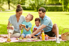 Family, Leisure And People Concept - Happy Mother, Father And Two Little Sons Having Picnic At Summer Park