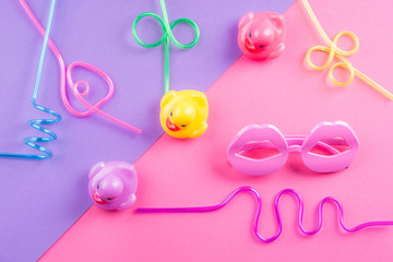 Wall Mural - Colorful funky summer flat lay with funny items - straws, rubber ducks, lip shape glasses. Pink and purple duotone background.