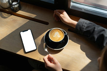 Young Woman With Cup Of Coffee And Smartphone In A Coffee Shop