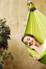 Portrait of smiling young woman relaxing in a hammock on the terrace house. Woman lying and covered with plaid in a hammock. Concept of rest, enjoyment, carefree.