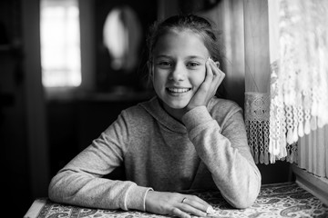 Wall Mural - Black and white portrait of a twelve-year-old cute girl sitting at the table.